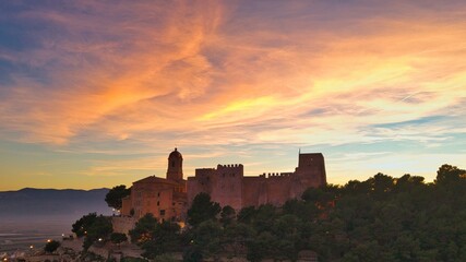 Fototapeta premium Sunset over Cullera castle and church on hilltop above Mediterranean coast – cinematic aerial view, Spain