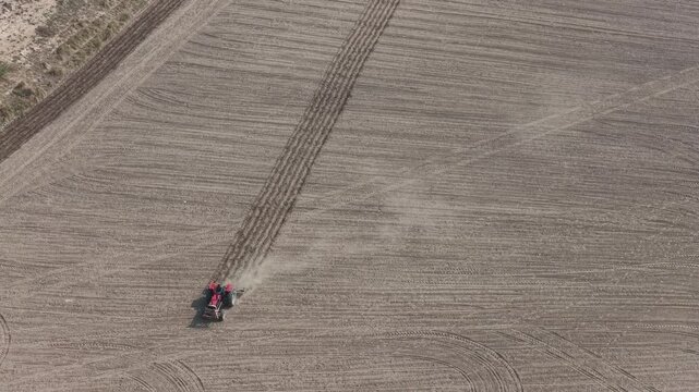 aerial drone footage of a Tractor harrowing a dry field, preparing the land for planting crops in a rural agricultural landscape during a sunny day High quality drone 4k footage