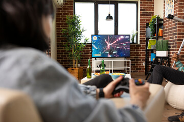 Young female gamer enjoys gaming session on television at home with friends. Diverse people sitting...
