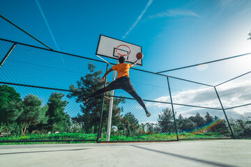 Athletic man jumping high to dunk a basketball on outdoor court under blue sky © Sasha