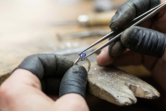 Jeweler carefully setting a blue sapphire gemstone into a silver ring with tweezers at a workshop.