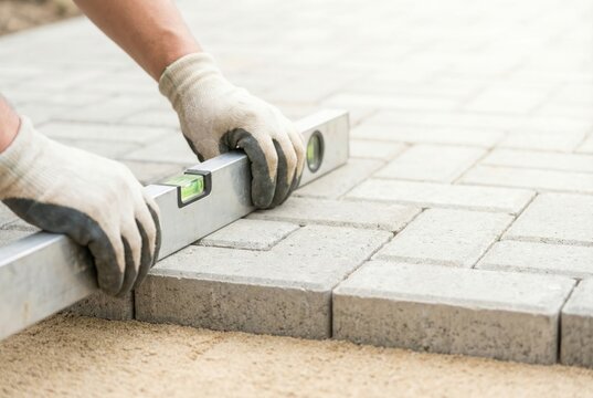 Landscaper using a spirit level to check the evenness of newly laid paving stones on a sand base.