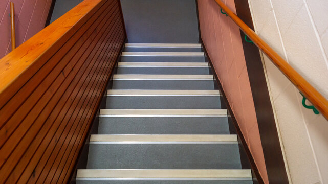Grey staircase with wooden railings and a wall painted half pink inside the building, view from above