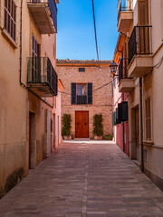 Fototapeta premium Narrow cobblestone alleyway winds through traditional Mediterranean stone buildings with wooden shutters in Alcudia's historic quarter, showcasing authentic Balearic Island architecture.