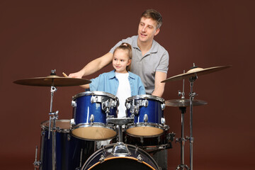 Little girl learning how to play drums with music teacher on brown background