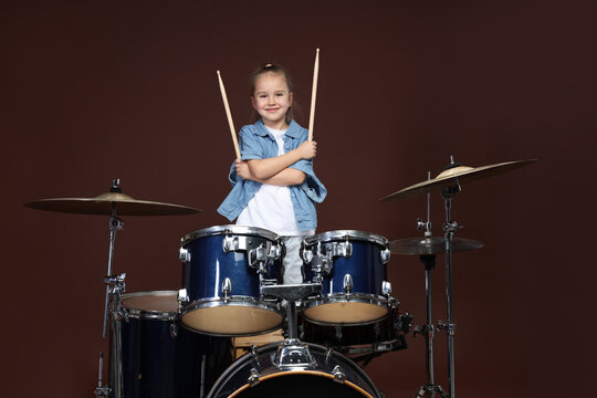 Little girl with drumsticks and drum kit on brown background