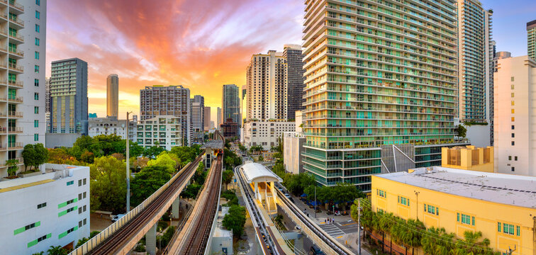 Aerial scene of Miami Brickell elevated railroad and passing commuter train between tall buildings and glowing sunset in Florida, USA