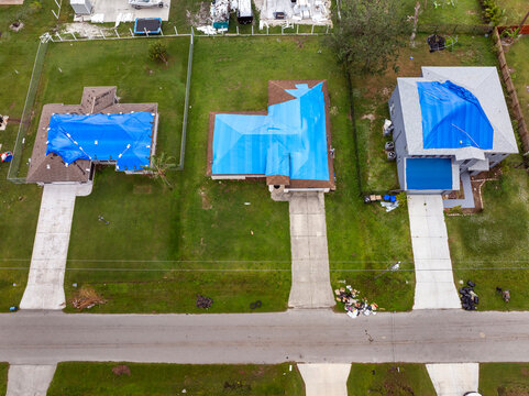 Top view of leaking house roof covered with protective tarp sheets against rain water leaks until replacement of asphalt shingles. Damage of building rooftop as aftermath of hurricane in Florida
