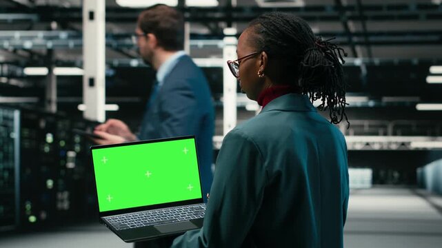 Green screen laptop in data center and AR tech used by technician to visualize and debug system errors. Server farm expert uses mockup notebook to run diagnostics on wireframe mesh gear, camera B