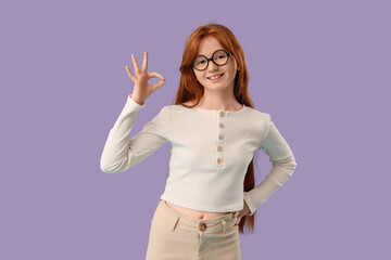 Teenage redhead girl showing OK gesture on lilac background
