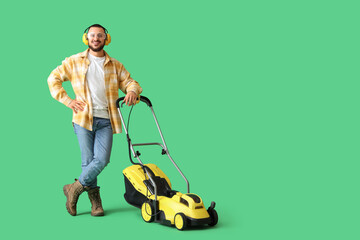 Young man in hearing protectors with lawn mower on green background