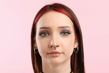 Fototapeta premium Portrait of beautiful young woman with different face piercings on pink background