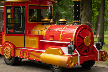 Colorful excursion train locomotive for children rides in city park with green trees background. Family entertainment, urban attraction, leisure activity and childhood recreation outdoors © Volha