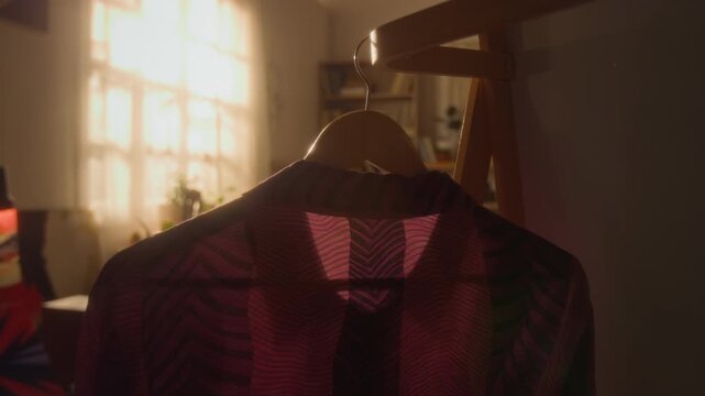 Cinematic detail shot of maroon vintage shirt on hanger in cozy bedroom lit by warm sunlight, no people, copy space