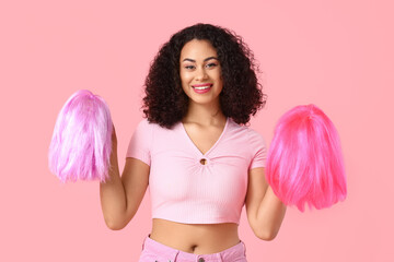Beautiful young African-American woman with different stylish wigs on pink background