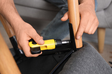 Man with screwdriver assembling armchair at home, closeup