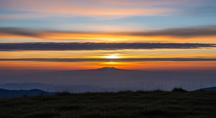 Obraz premium Vibrant sunset over a silhouetted mountain range with stunning layered clouds and golden hour colors.