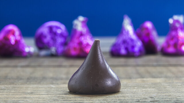 NORWALK, CT, USA - FEBRUARY 24, 2026: A single Hersheys chocolate kiss stands on a wooden table. Colorful wrapped chocolates are in the background.  