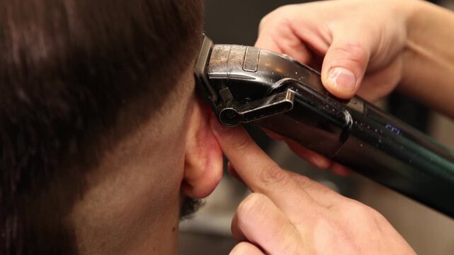 Stylist cutting man's hair with clipper in barbershop, closeup