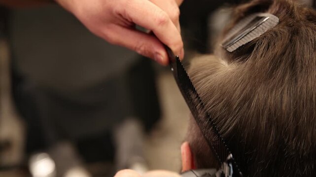 Stylist cutting man's hair with clipper in barbershop, closeup
