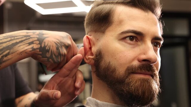 Stylist cutting man's hair with clipper in barbershop, closeup