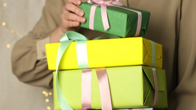 Woman with stack of beautiful gift boxes showing one against grey background with blurred lights, closeup