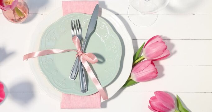 Stylish table setting with floral decor on white wooden background, flat lay. Camera moving left