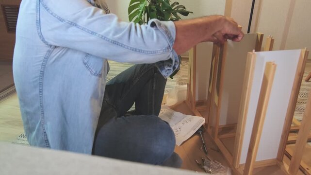 Unrecognizable person sitting on the floor assembling new flat pack furniture following the instructions