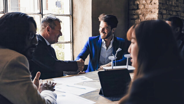 Multigenerational business people shaking hands in sustainable innovation meeting - Green renewable project agreement concept