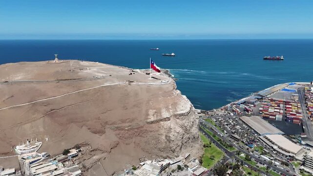 Aerial 4K view of Morro de Arica with Chilean flag waving, sunny day over the Pacific Ocean coast and historical landmark. Chile