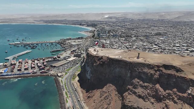Aerial 4K view of Morro de Arica with Chilean flag waving, sunny day over the Pacific Ocean coast and historical landmark. Chile