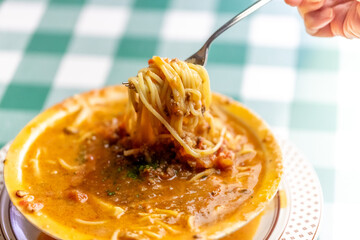 ひき肉の旨味が溶け出したスープにパスタを絡め、ボロネーゼのスープパスタをフォークで高く持ち上げるリフトアップ。麺に絡むソースの質感や、イタリアンレストランのランチ・ディナーメニューを伝える販促・広告用素材に。 | Lifting Bolognese soup pasta with a fork to show the savory meat sauce and noodles.