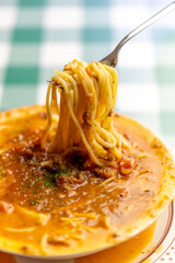 ひき肉の旨味が溶け出したスープにパスタを絡め、ボロネーゼのスープパスタをフォークで高く持ち上げるリフトアップ。麺に絡むソースの質感や、イタリアンレストランのランチ・ディナーメニューを伝える販促・広告用素材に。 | Lifting Bolognese soup pasta with a fork to show the savory meat sauce and noodles.