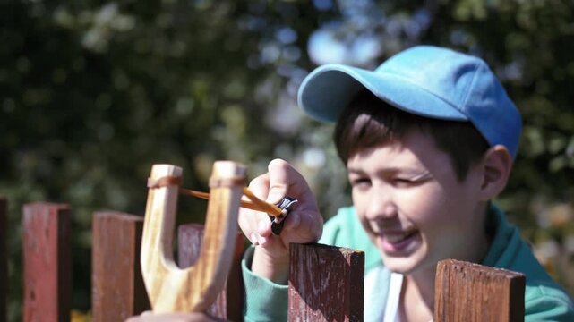Sunny Playtime: Boy Aiming with Slingshot and Hiding Behind Fence on a Bright Summer Day