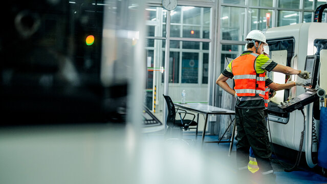 Three engineers program an industrial robot or 5-axis CNC machine using an AI interface. The team manufactures advanced microchips or high-tech components in a smart factory.