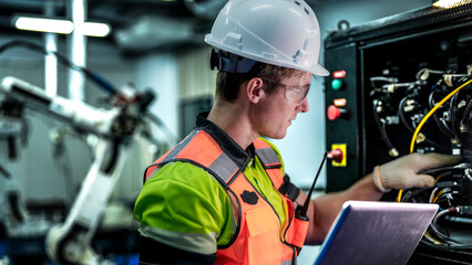 A robotics engineer uses a laptop to run diagnostics on an AI system. He is checking the hardware, wiring, and high-tech sensors of an industrial robot.