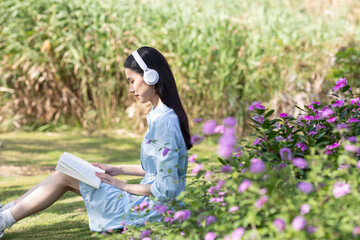 Fototapeta premium A young Chinese woman sitting on the grass reading a book outdoors