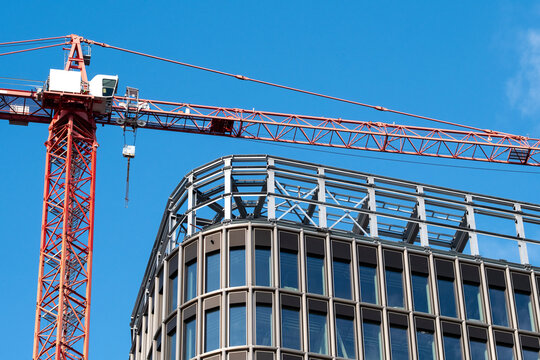 High crane over modern urban building rooftop under blue sky showing steel structure and architecture during active construction industry development
