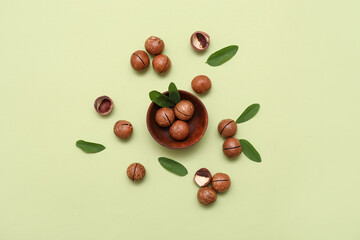 Naklejka premium Wooden bowl with tasty macadamia nuts and leaves on green background