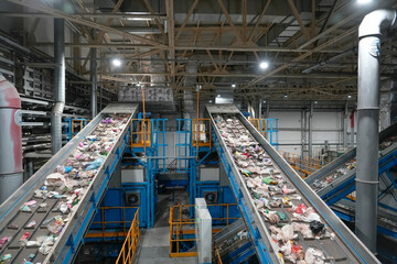 Fototapeta premium Waste sorting facility operates by separating various types of refuse for recycling. Conveyors carry debris, showcasing an assortment of discarded materials in a clean industrial environment
