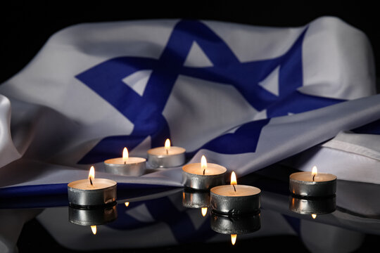 Burning candles and large flag of Israel on dark background. Holocaust Remembrance Day