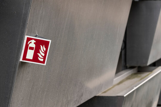 Industrial metal wall detail showing red warning sign and fire extinguisher safety icon for emergency preparedness and security closeup