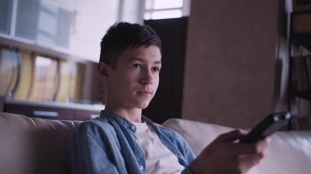 Evening Leisure: Young Boy Relaxing on the Couch, Channel Surfing on TV