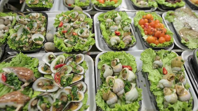 Street Market Snails On Lettuce Trays With Cherry Tomatoes, Assorted Clams And Bitesized Shell Portions, Vendor Arranging Plates For Customers, Herb And Chili Garnish, Close Overhead Shot
