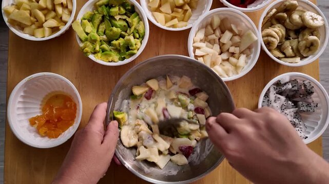 A woman has added sour cream dressing to a fruit salad and is mixing all the ingredients