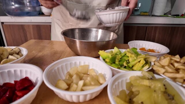 A woman adds a dragon fruit, prepares a fruit salad, putting pieces of different fruits into one bowl