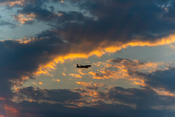 Obraz premium Airplane flying through clouds at sunset
