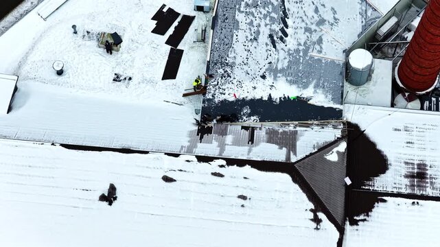 Roofers repairing commercial building roof after snow, maintenance specialists at height