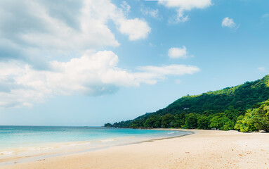 Tropical beach curving along turquoise bay, lush hillside backdrop.