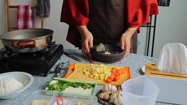 Hands home Chef grinding garlic and spices in stone mortar (cobek) for Indonesian corn fritters (Bakwan Jagung)